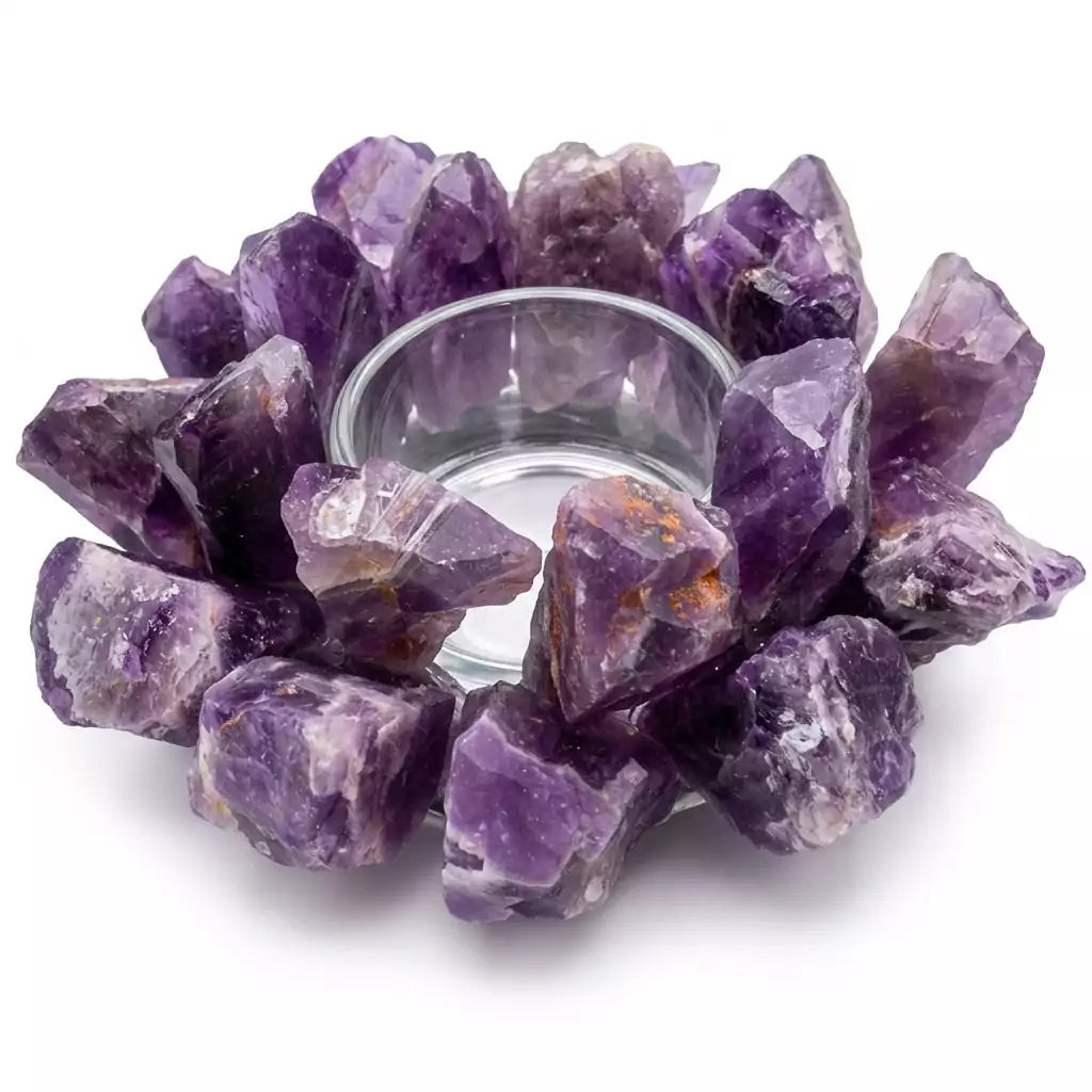A circular arrangement of raw amethyst crystals surrounds a clear glass candle holder. The crystals are various shades of purple, creating a decorative and natural look.