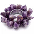 A circular arrangement of raw amethyst crystals surrounds a clear glass candle holder. The crystals are various shades of purple, creating a decorative and natural look.