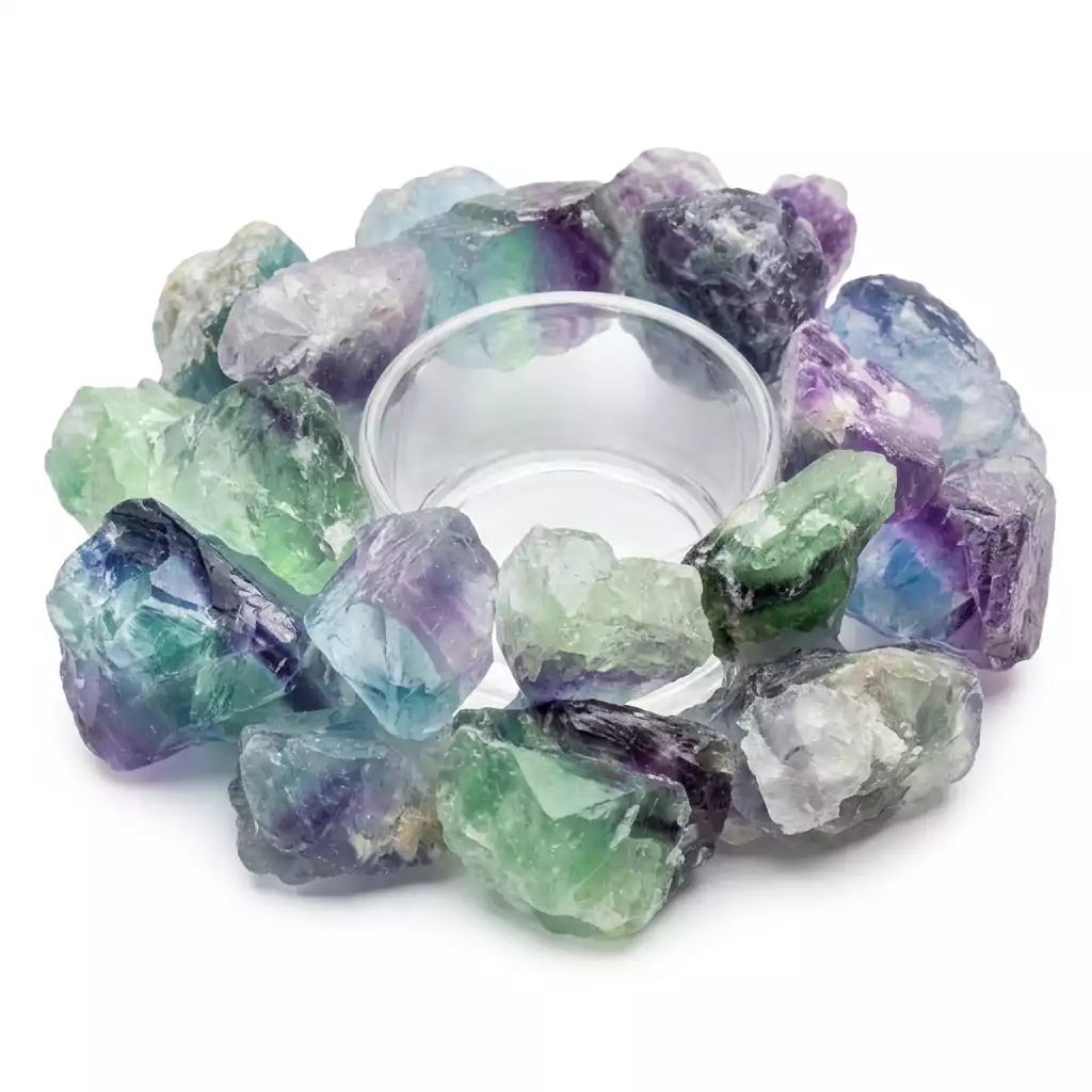 A circular arrangement of colorful fluorite crystals in shades of green and purple surrounds a clear glass dish. The crystals are rough and unpolished, showcasing their natural beauty.