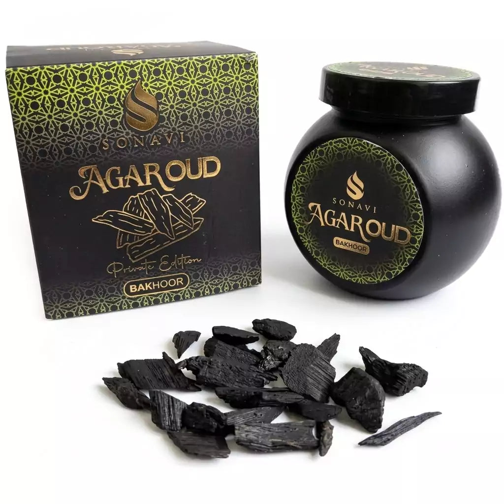 Black jar of Sonavi Agar Oud bakhoor incense chips next to its decorative box, with small dark agarwood chips scattered about — 40g natural agarwood resin blend.