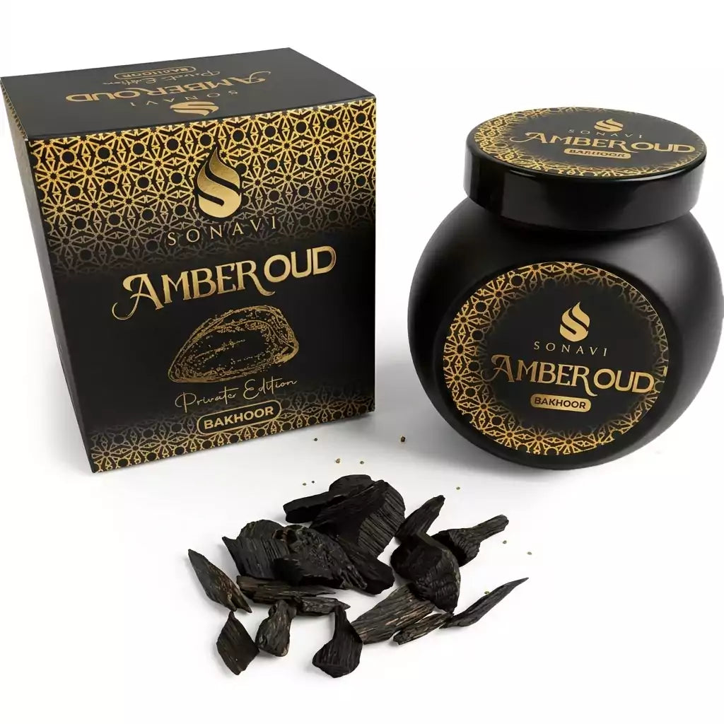 Black jar of Sonavi Amber Oud bakhoor incense chips with decorative gold lid, next to its matching box, with small oud wood pieces scattered on the surface — 40g warm amber and oud resin blend for ritual and meditation.