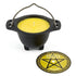 Small black cast iron cauldron with a yellow citronella candle inside and a circular holder stand, designed for outdoor ritual use and insect repelling patio altars.