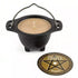 Small black cauldron-shaped ritual candle with beige wax interior accompanied by a round pentagram design label, patchouli scented for Wiccan altar use