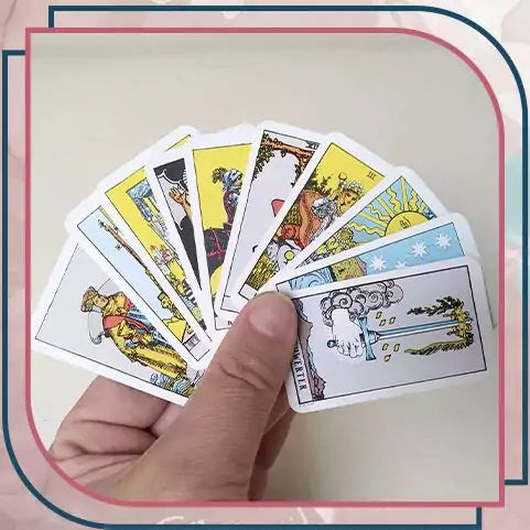 Hand holding a spread of miniature Rider-Waite tarot cards — showing colorful illustrated cards fanned out from the mini pocket edition deck for scale.