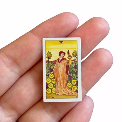 Hand holding a single Tiny Universal Waite Tarot card showing a robed figure in a sunlit meadow.