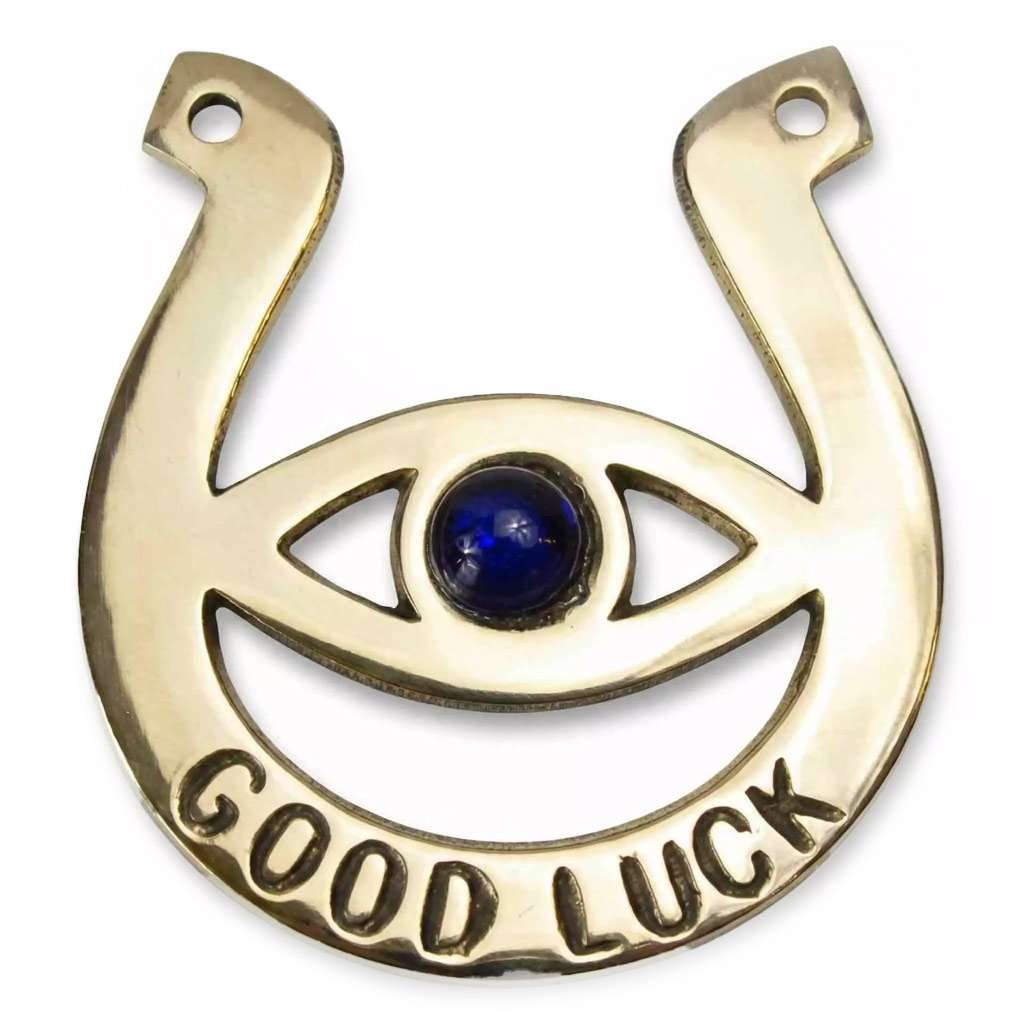 Golden brass-tone horseshoe charm with a central blue evil eye and "GOOD LUCK" inscription at the base, for wall hanging or altar placement.
