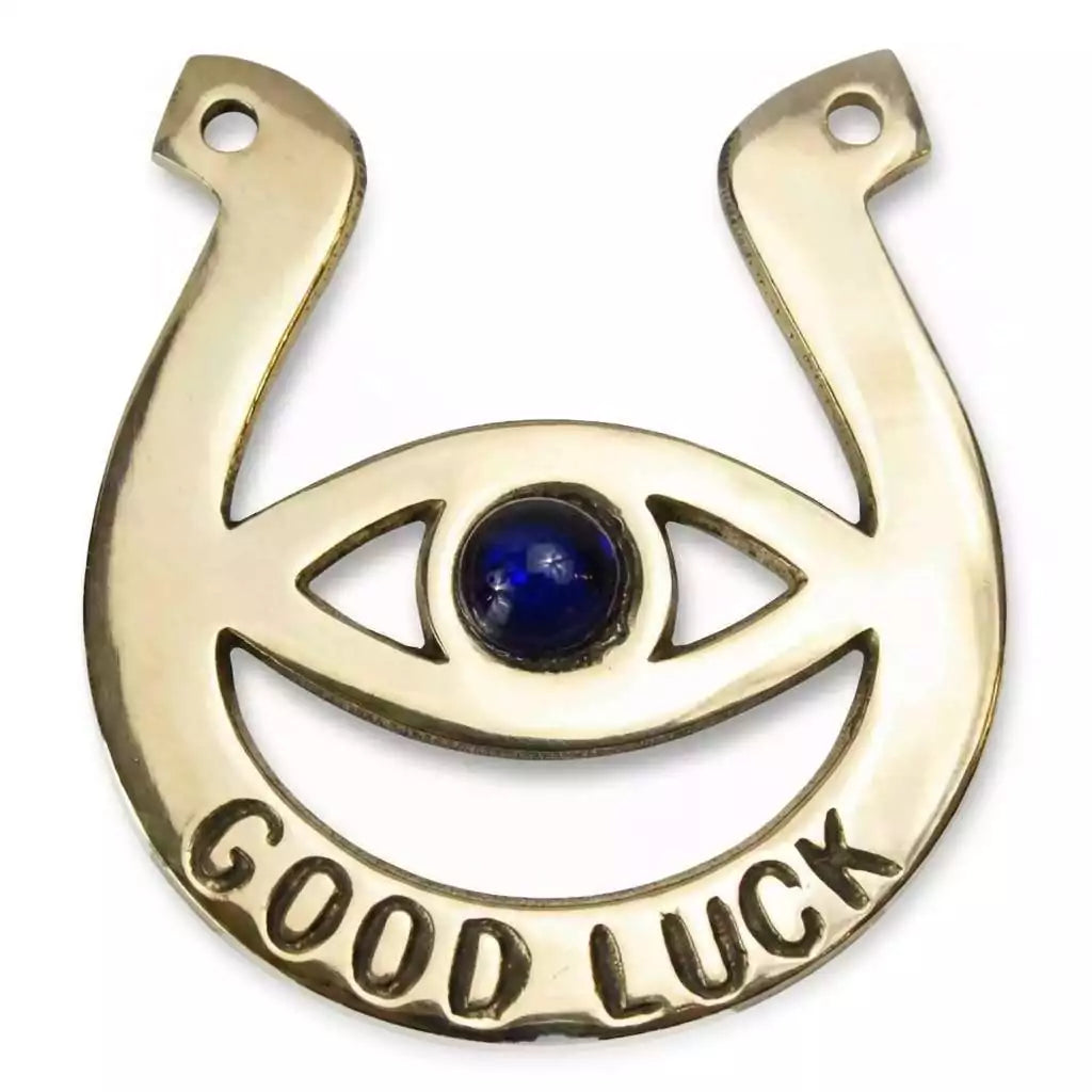Golden brass-tone horseshoe charm with a central blue evil eye and "GOOD LUCK" inscription at the base, for wall hanging or altar placement.