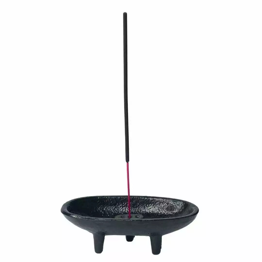 Black cast iron incense holder with a stick of incense burning — showing the cauldron burner in active ritual use.