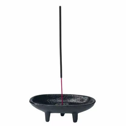 Black cast iron incense holder with a stick of incense burning — showing the cauldron burner in active ritual use.