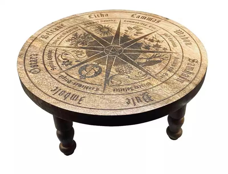Round carved wooden altar table with a wheel-of-the-year compass design, sabbat symbols, and directional markings carved into the surface — 11¾-inch diameter.