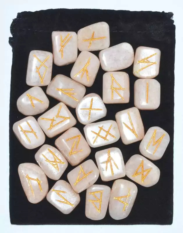 Moonstone rune set displayed on dark fabric showing golden-tinted rune symbols on polished stones — 25-piece Elder Futhark collection.