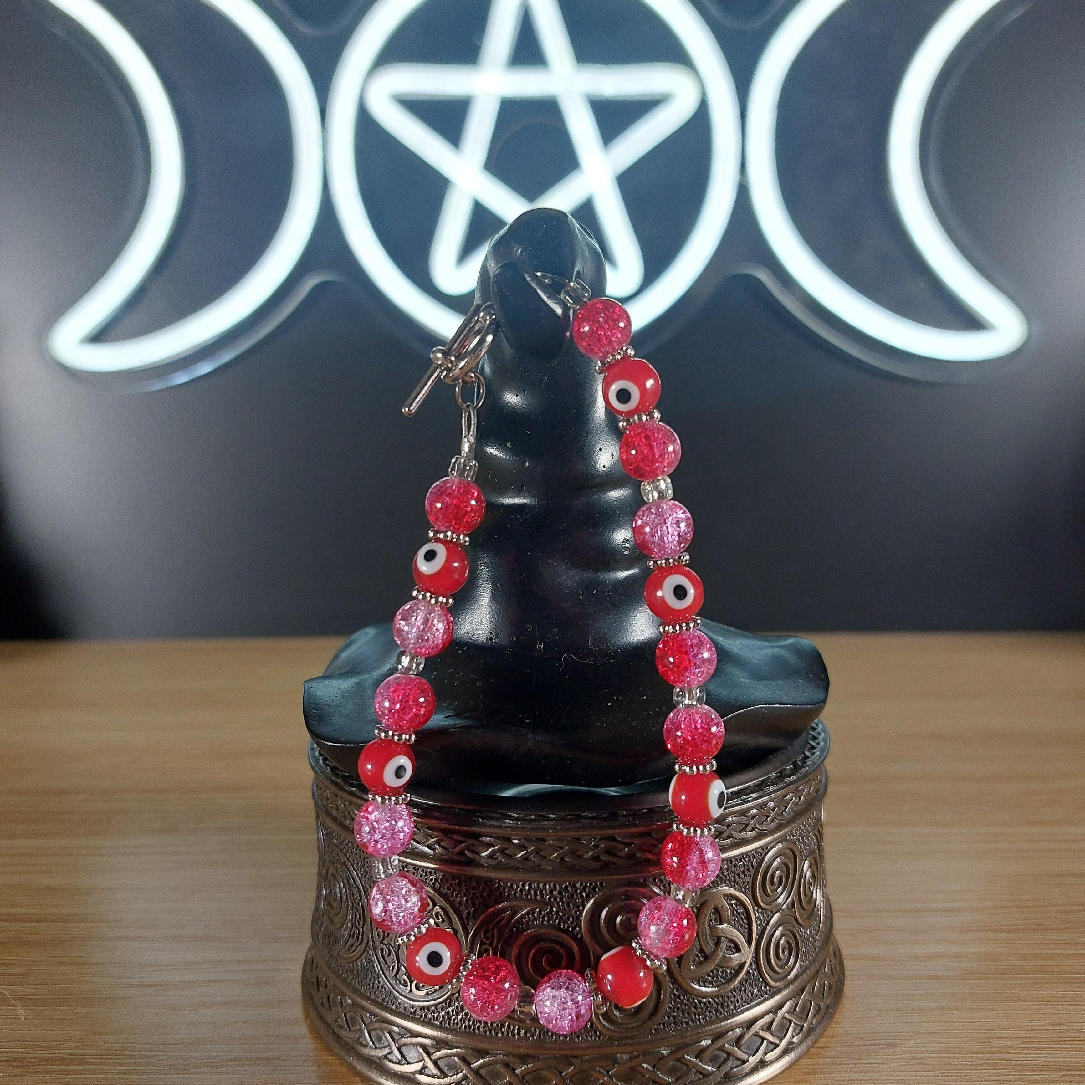 Pink and red glass bead bracelet with evil eye charms and a toggle clasp.