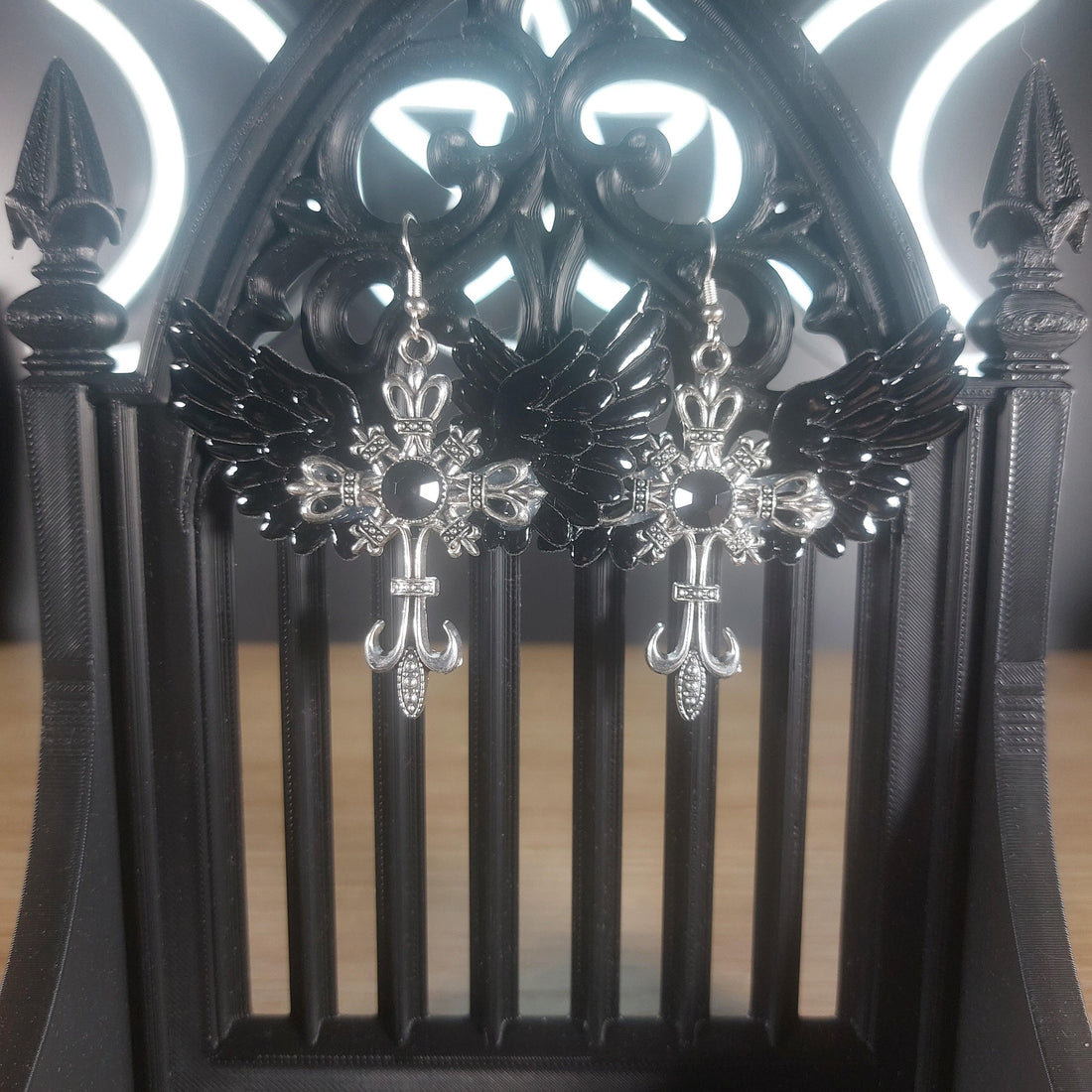 Black winged silver-tone cross dangle earrings with intricate gothic details.