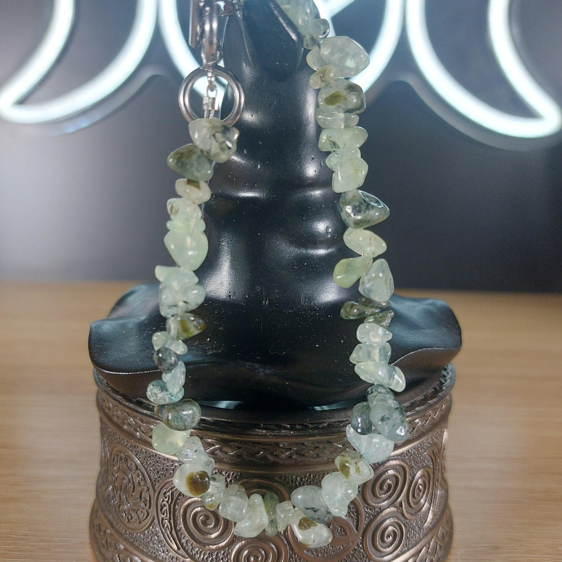 Pale green prehnite crystal chip bracelet with a silver stainless steel toggle clasp, displayed on a black stand.