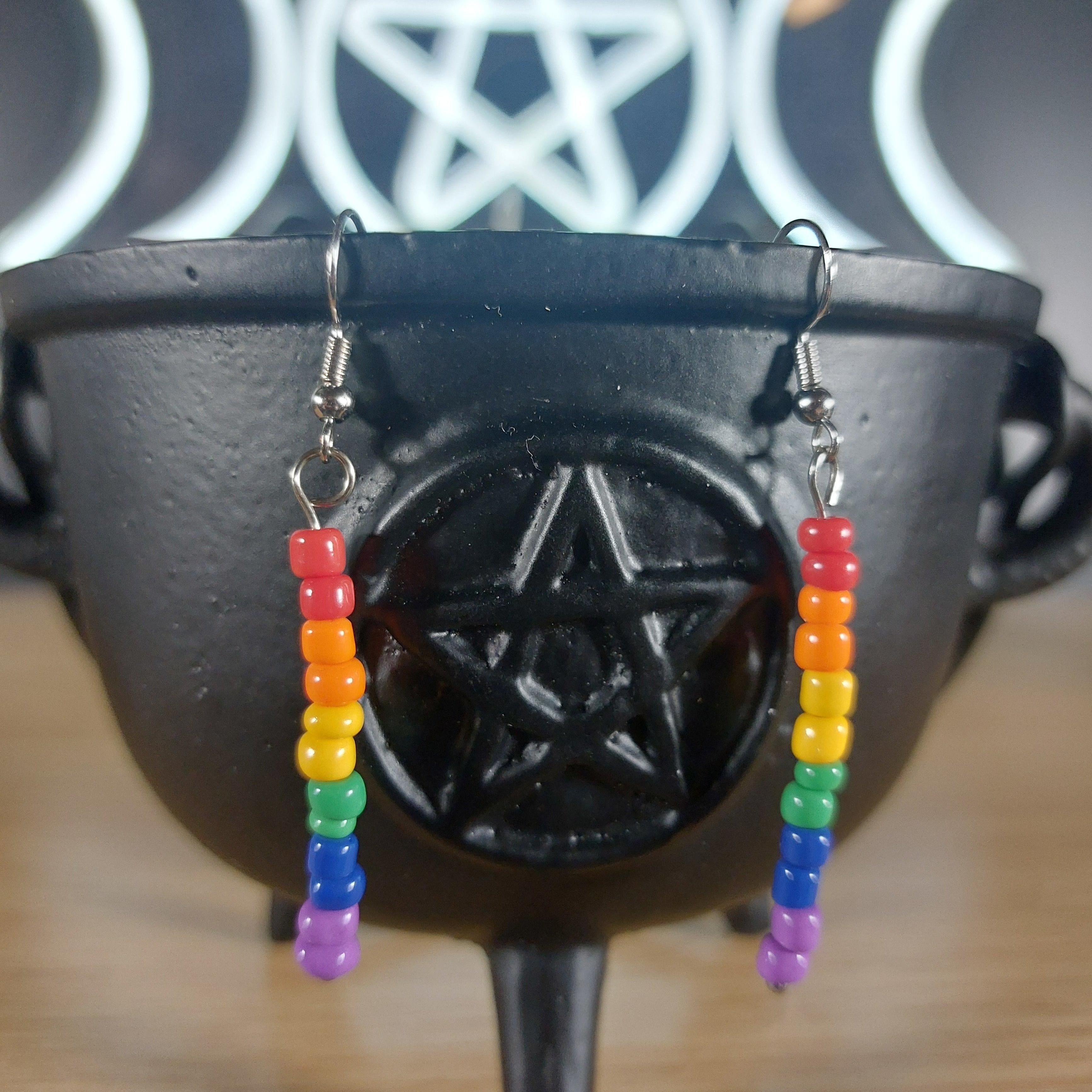 Rainbow seed bead dangle earrings with silver hooks, displayed on a black cauldron.