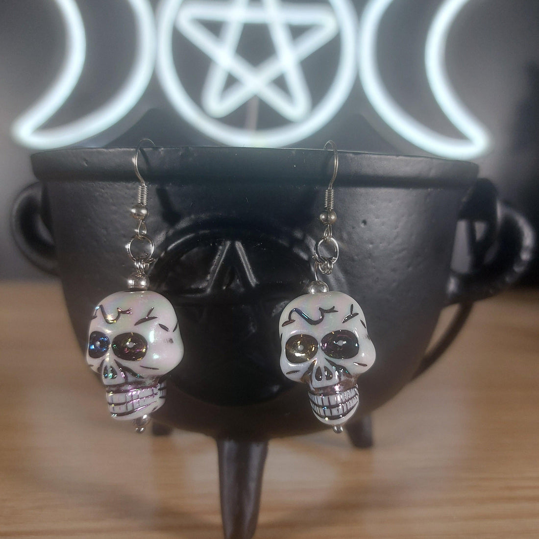 White plastic skull dangle earrings with rainbow accents, hanging from silver hooks.