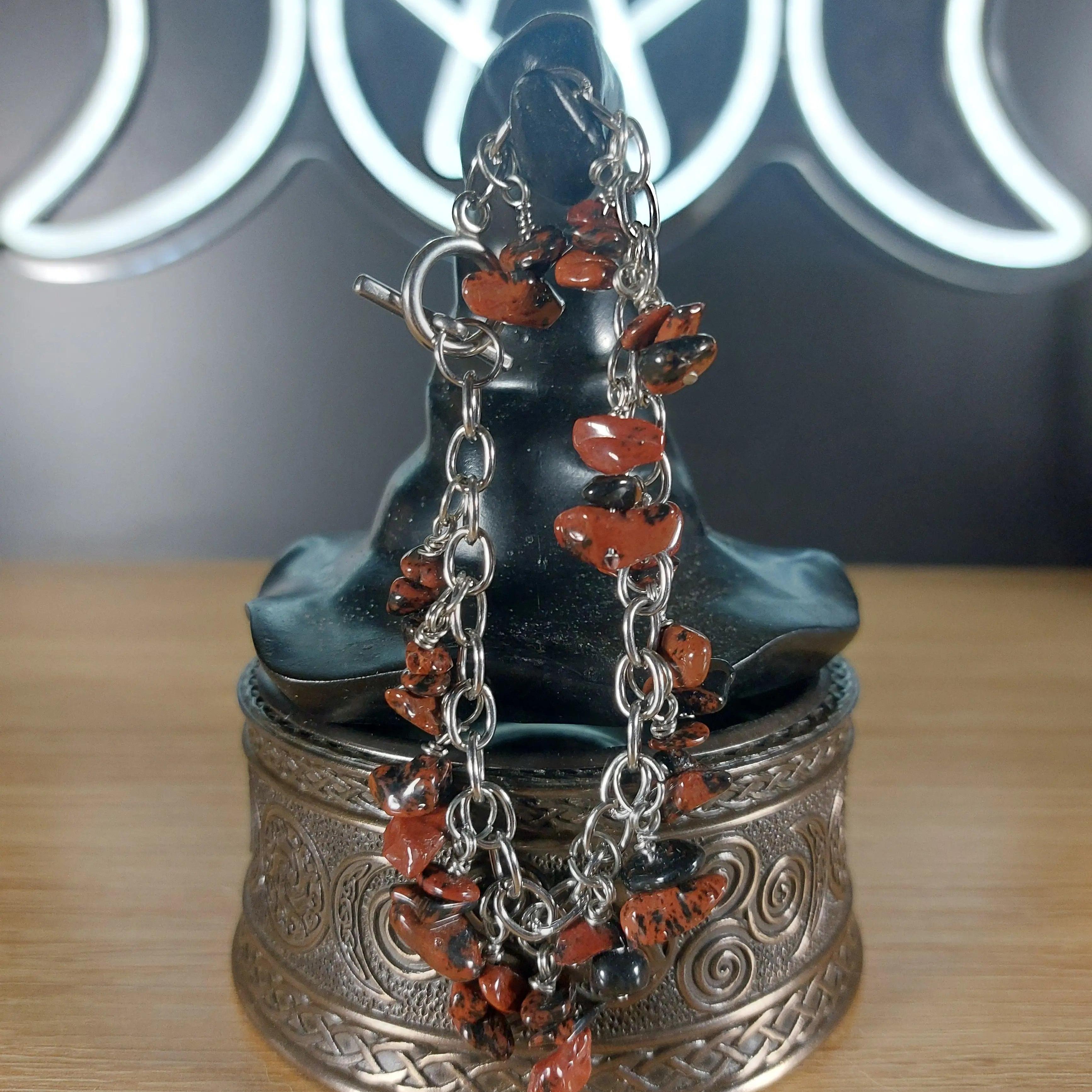 Mahogany obsidian chip bracelet with stainless steel chain on a dark display bust.