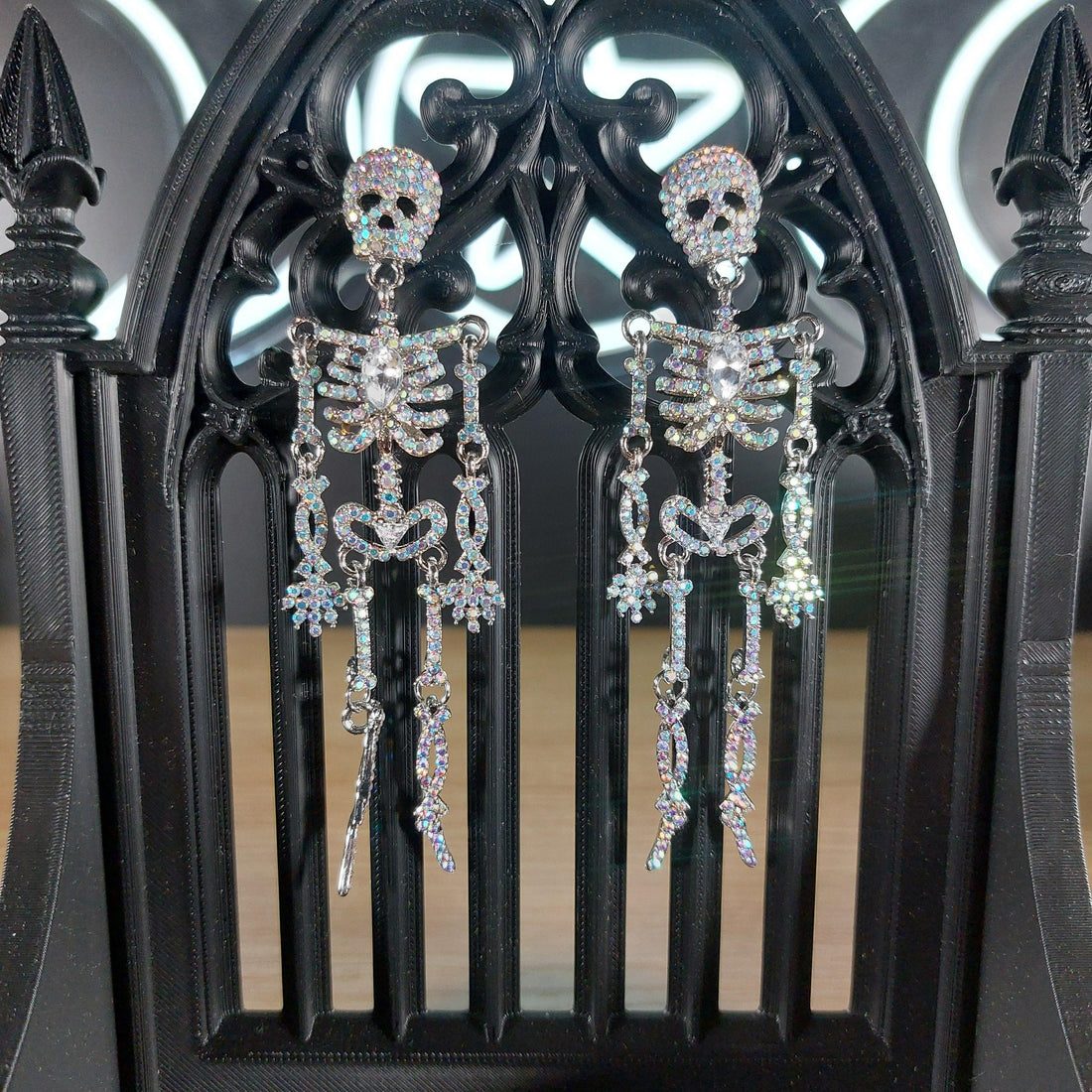 Sparkling rhinestone skeleton dangle earrings on a black gothic stand.