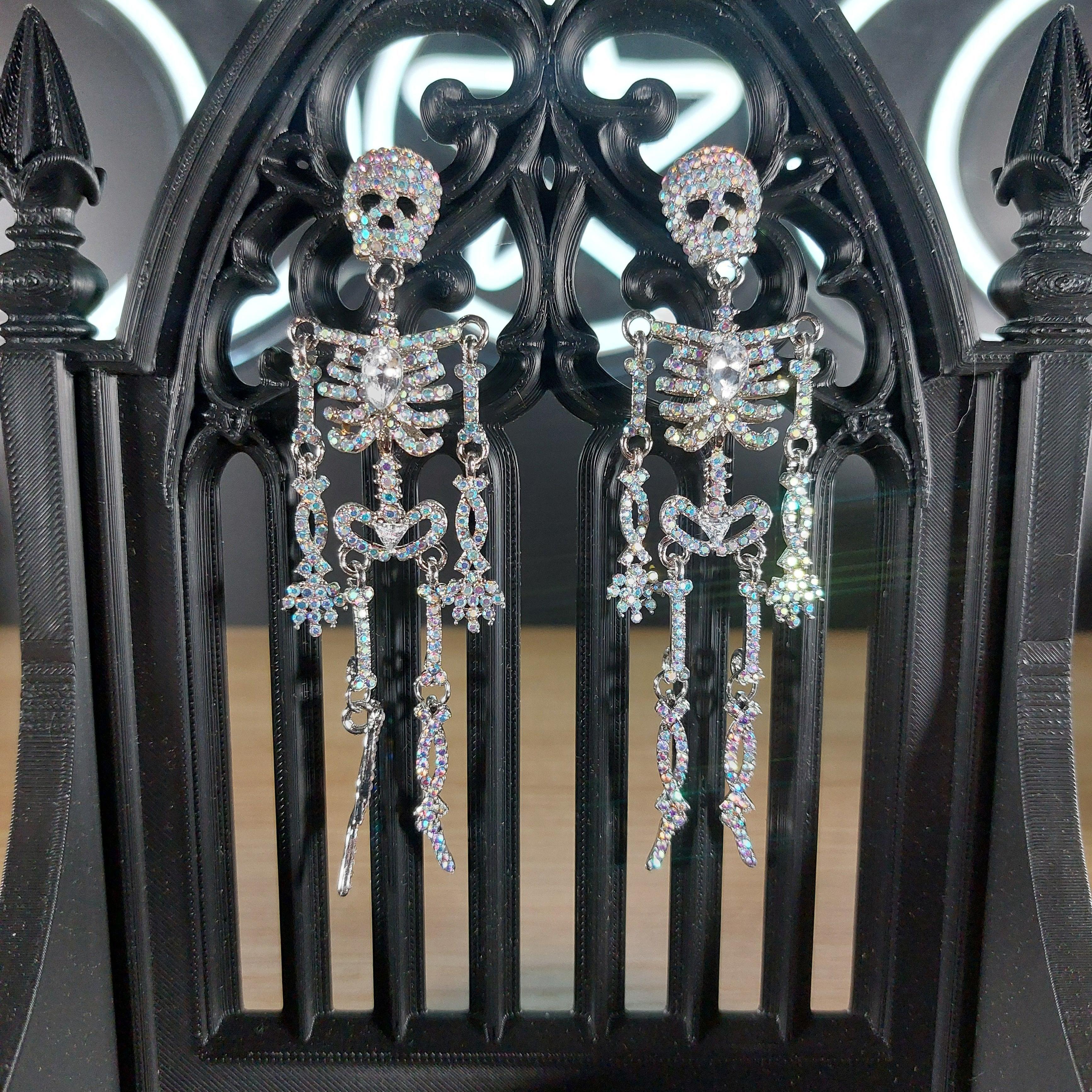 Sparkling rhinestone skeleton dangle earrings on a black gothic stand.