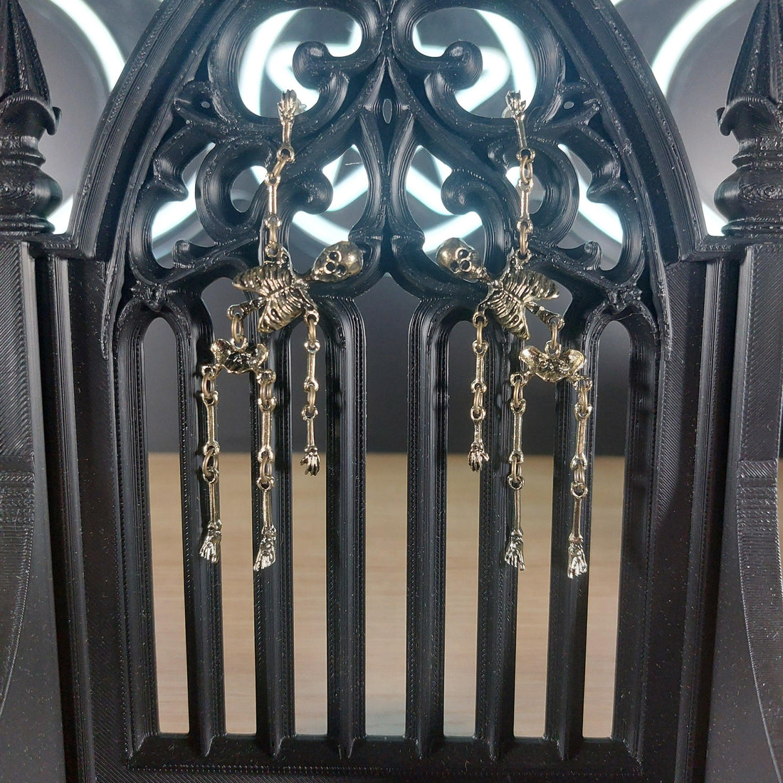 Antique gold tone skeleton dangle earrings on a black gothic arch display.