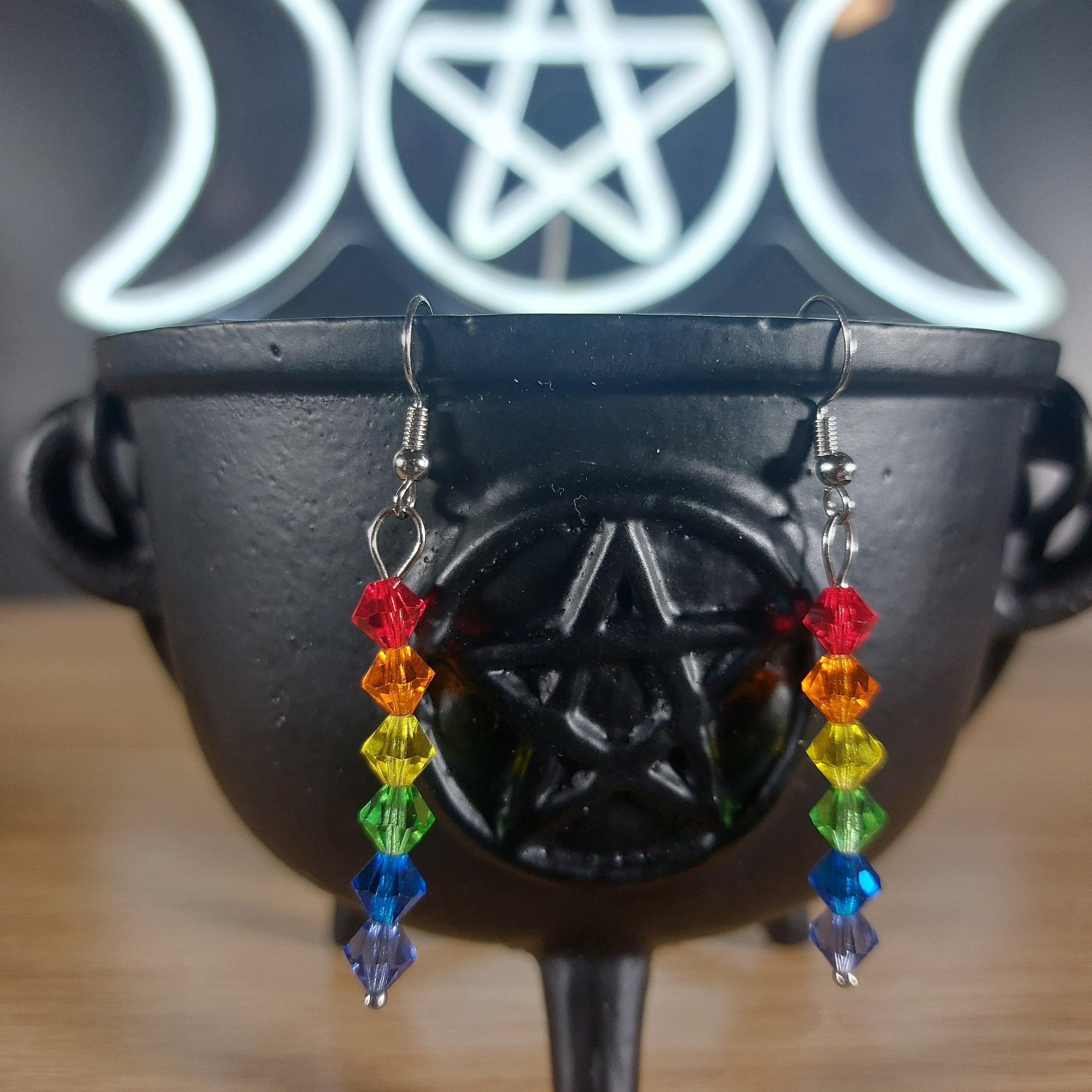 Rainbow plastic bicone dangle earrings on a black cauldron with a glowing triple moon and pentagram symbol.