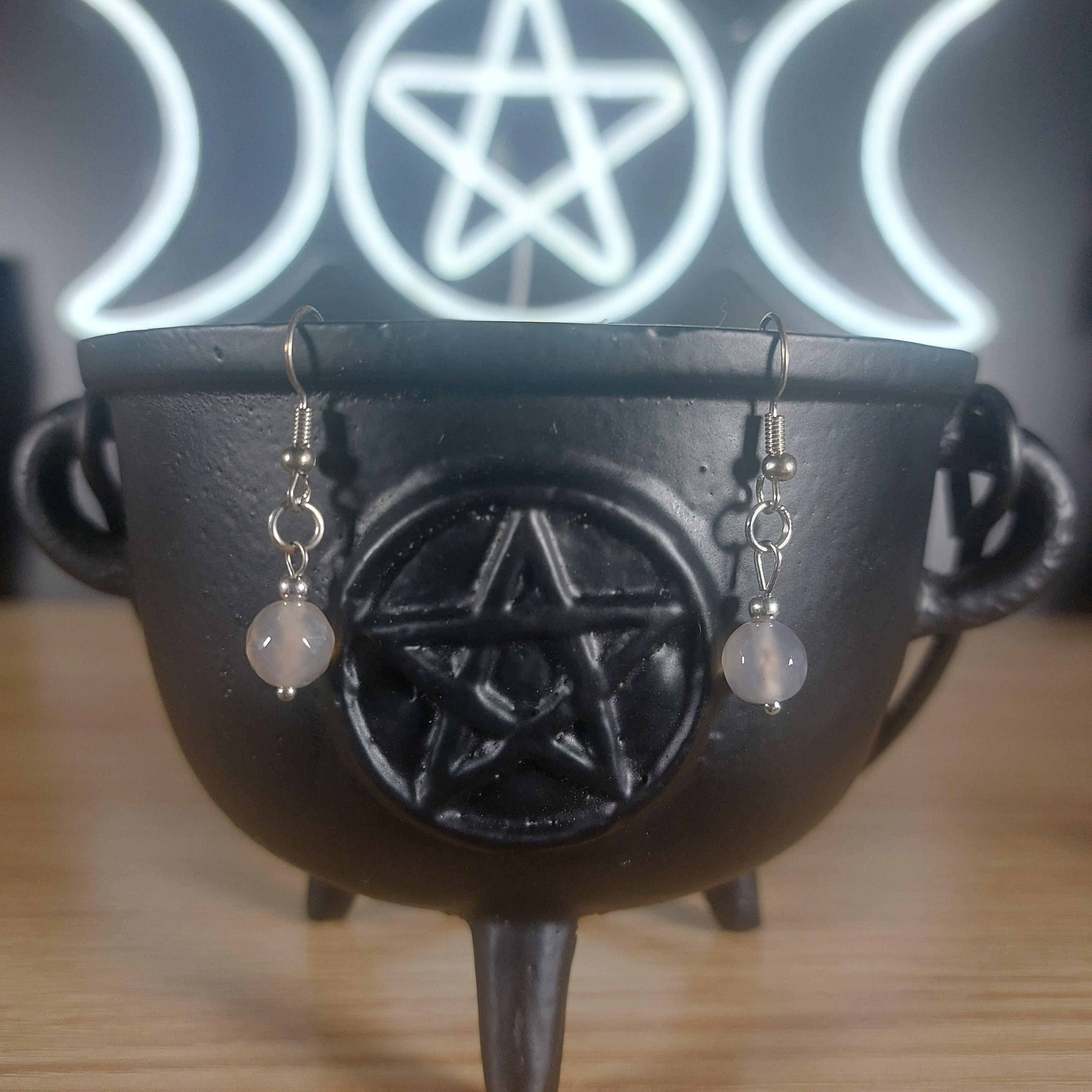 Smoky quartz crystal beaded dangle earrings in a black cauldron, with a glowing Triple Moon symbol in the background.