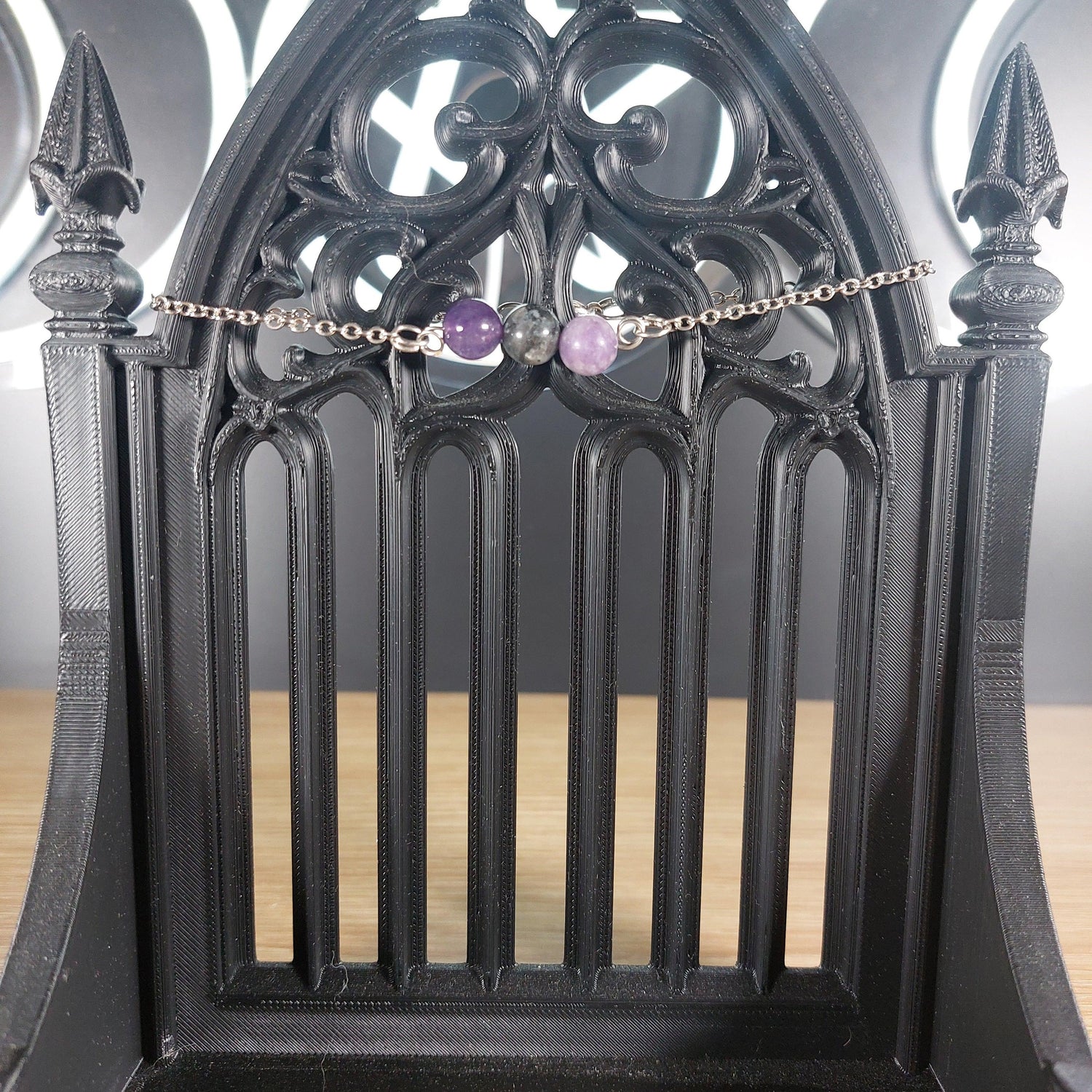 Silver tone chain bracelet with labradorite, amethyst, and lepidolite beads on a gothic black stand.