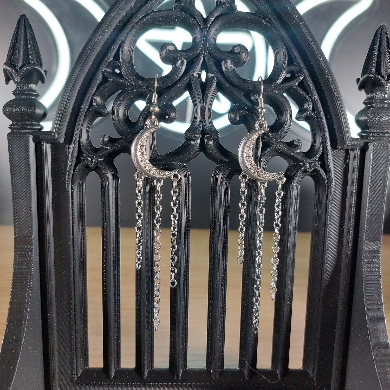 Silver tone moon dangle earrings with rhinestones and three chains, displayed on a gothic black stand.