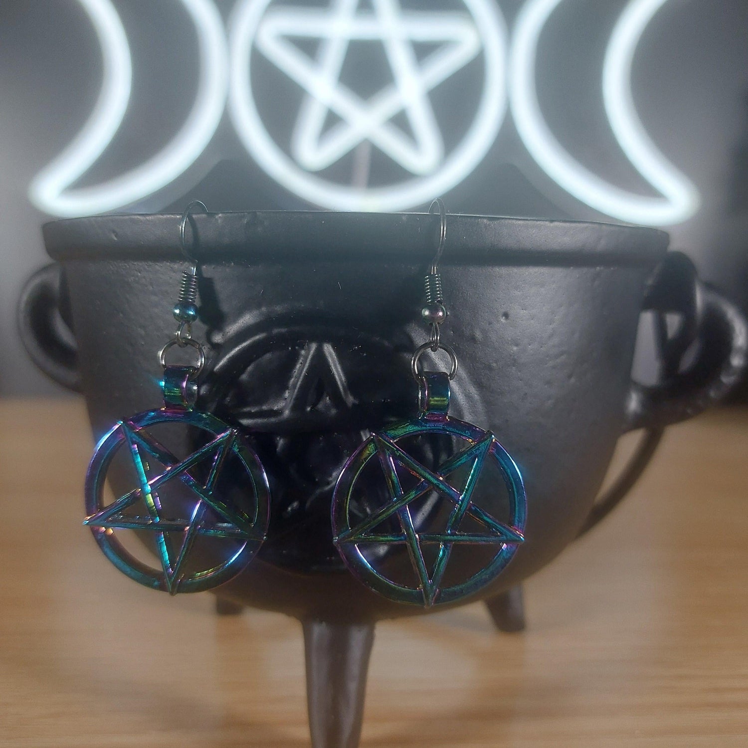 Rainbow iridescent inverted pentagram dangle earrings on a black cauldron.