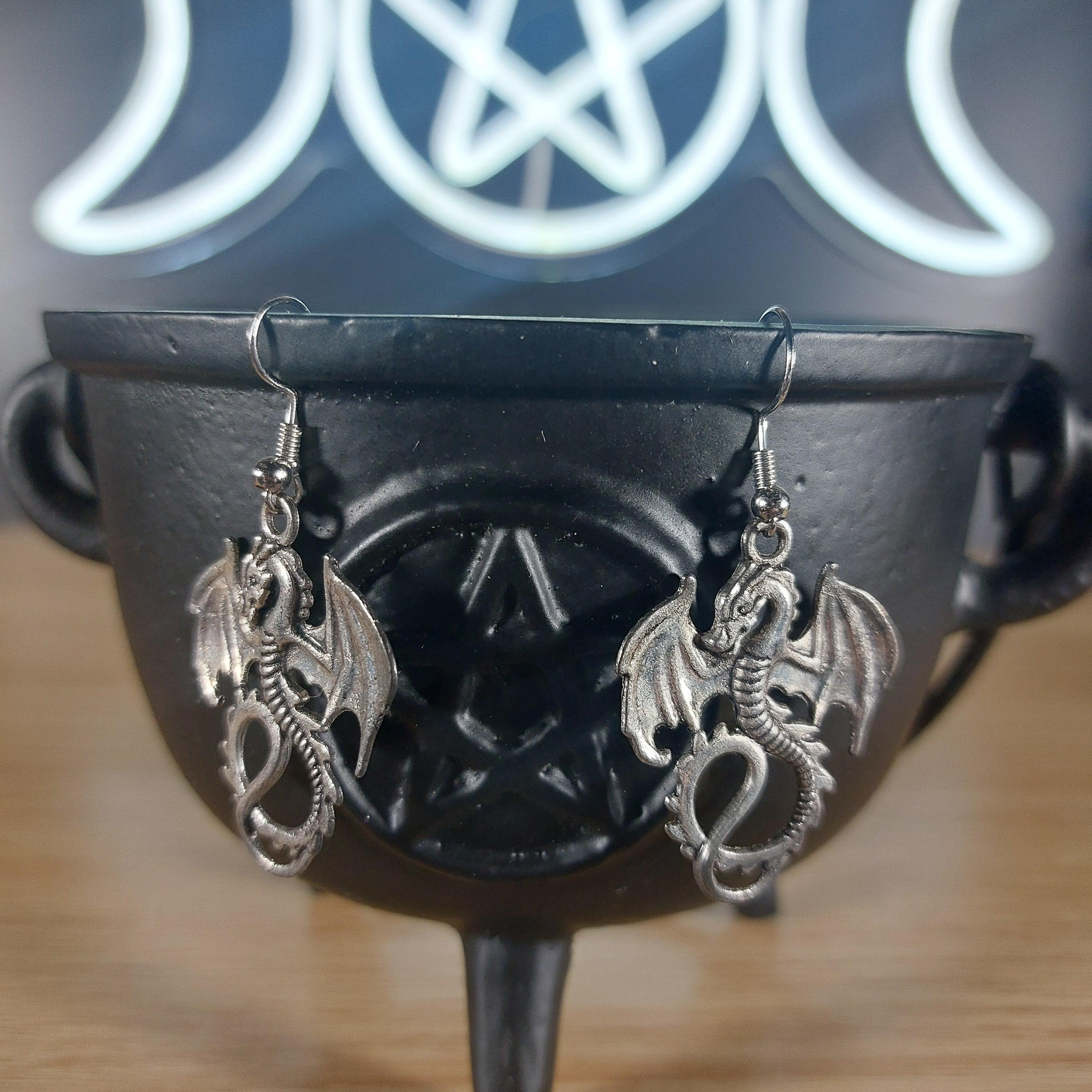 Antique silver tone dragon dangle earrings hanging from a black cauldron.